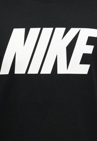 Έντονο λευκό κείμενο με λογότυπο NIKE σε μαύρο υφασμάτινο φόντο, με μεγάλα κεφαλαία γράμματα σε αθλητική, πλάγια γραμματοσειρά.