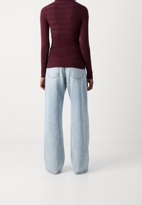 Haut ajusté bordeaux avec des rayures horizontales, associé à un jean en denim bleu clair à jambes larges. Coupe droite avec poches arrière et ourlets légèrement effilochés.