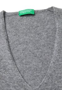 Szary sweter w serek z zieloną metką "United Colors of Benetton" wszytą w dekolt na białym tle.