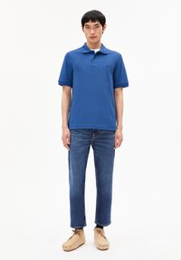 Blaues Polohemd mit kurzen Ärmeln, lockere Passform, kombiniert mit blauen Jeans und hellen Mokassins, schlichtes Design.