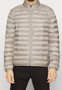 Giacca puffer grigia chiara con zip frontale, colletto a coste, design trapuntato e polsini elasticizzati. Sono visibili anche tasche laterali.