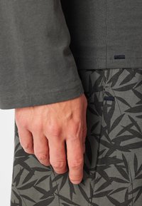 Camicia a maniche lunghe di color verde scuro abbinata a pantaloni grigi con un motivo a foglia nera. La camicia ha un collo a giro e orli cuciti.