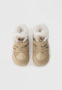 Beige støvler med en myk hvit pelskrage og borrelåser. Designet inkluderer sømdetaljer og et leopardmønstret element på stroppen.