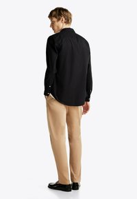 Chemise noire à manches longues avec un col boutonné. Pantalon beige clair et mocassins noirs. Tissu lisse avec une coupe ajustée.