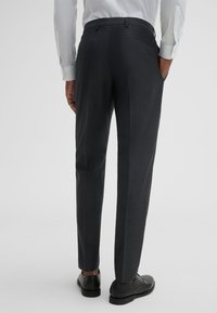 Graumelierte, maßgeschneiderte Hose mit dezentem Muster, schlanker Passform, Seitentaschen und glatter Textur, kombiniert mit schwarzen Lederschuhen.