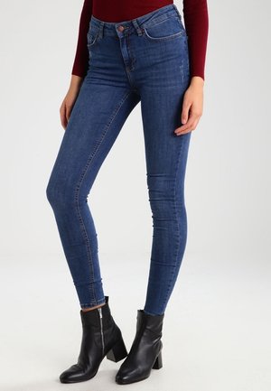 Pantalones vaqueros azules ajustados con cintura alta, con un diseño clásico de cinco bolsillos y detalles de costura sutiles, combinados con botas negras hasta el tobillo.
