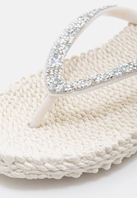 Witte geweven teenslipper met sprankelende strass-besierde bandjes en een gestructureerde gevlochten zool.