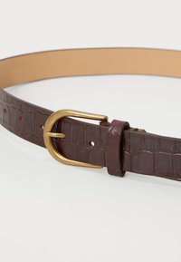 Ceinture en cuir marron avec une texture crocodile, dotée d'une boucle en laiton et de trous pour ajustement. Doublure et bords en cuir lisse couleur fauve.