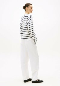 Biała i granatowa w paski bluzka z długim rękawem i obniżonymi ramionami, w połączeniu z białymi spodniami o szerokich nogawkach i czarnymi butami wsuwanymi.