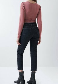 Tight ribbad rosa långärmad topp i kombination med högmidjade svarta jeans. Jeans har raka ben och synliga bakfickor. Svarta anklar stövlar.