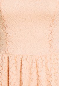 Robe en dentelle pêche avec motif floral, surface texturée et jupe évasée. Dispose d'un corsage ajusté et d'une taille froncée.