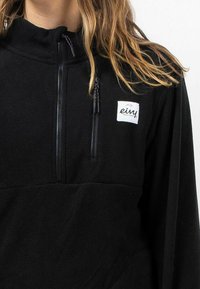 Zwarte fleece pullover met hoge kraag, rits aan de voorkant en merkpatch. Heeft een gestructureerde stof en contrasterende ritslussen.