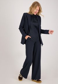 Marineblauwe broek en blazer set, met een gestructureerde blouse en een wijde pijpdesign. Accenten van een gladde afwerking en een relaxte pasvorm.