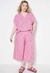 Roze geprinte co-ord set met een top met korte mouwen en wijdvallende culottes met een geometrisch ontwerp; gecombineerd met roze sandalen.