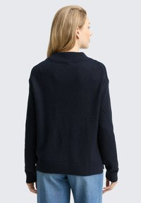 Granatowy sweter dzianinowy o teksturowanym wzorze, z prążkowanym kołnierzem i mankietami oraz bocznymi rozcięciami. Zaprojektowany w luźnym fasonie z długimi rękawami.