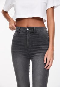 Mustat, korkeavyötäröiset farkut, joissa haalistunut viimeistely, etutaskut, metallinen napin suljin ja vyölenkit. Sileä rakenne.