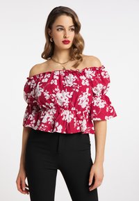 Rød blomstret off-the-shoulder bluse med hvide blomster, flæseærmer og peplum-design. Båret med sorte tætsiddende bukser.