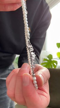 Pulseira de pérolas com ferragens prateadas e uma inscrição em letra cursiva. Pérolas redondas e lisas alternadas com detalhes metálicos.