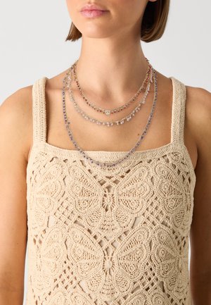 Meerdelige ketting met gouden kettingen en rode, paarse en lila kralen, gedragen met een beige gehaakte top die een vlinderpatroon toont.