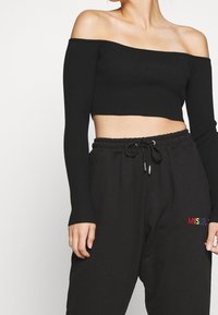 Svart kort off-the-shoulder tröja med ribbad textur och långa ärmar, i kombination med svarta sweatpants som har flerfärgad "MISSGUIDED" brodyr.
