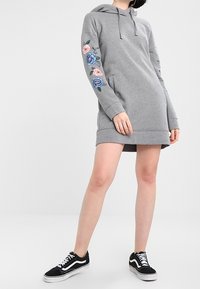 Grå hoodie-klänning med blommotiv i blått och rosa på ärmarna, med en framficka och justerbar dragsko i huvan.