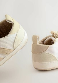 Sneakers beige e bianchi con tessuto testurizzato, dettagli in camoscio e un rivestimento interno con motivo. Presentano un tassello sul tallone per una facile indossabilità.