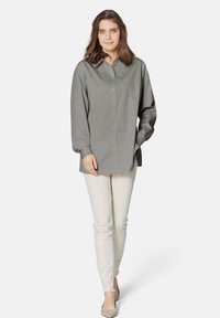 Lichtgrijze knop-up shirt met een kraag, lange mouwen en een rechte snit, gecombineerd met strakke crème kleurige broeken en grijze hakken.