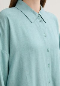 Camisa de botones azul claro con cuello, hecha de una tela suave, con una textura lisa y botones a juego.
