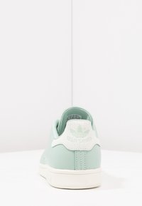 Sneaker verde chiaro con tomaia in pelle liscia, dettagli in gomma bianca sul tallone e logo. Presenta una punta tonda e una suola in gomma piatta.
