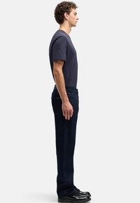 Ciemnoniebieskie dżinsy z denimu i ciemny t-shirt, profil boczny, casualowy krój, gładka faktura, prosty design, dobrane do czarnych butów.