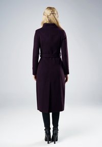Długi fioletowy wełniany płaszcz z kołnierzem, z paskiem w talii i rozcięciem z tyłu; połączony z dopasowanymi czarnymi spodniami i czarnymi botkami na obcasie.