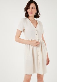 Light beige short-sleeve dress with a V-neck, button-down front, and a flared skirt. Made from a soft, textured fabric.