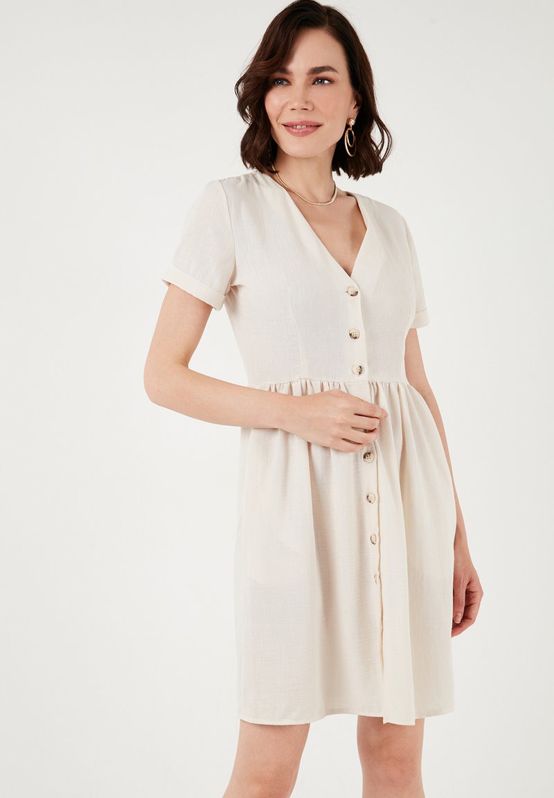 Light beige short-sleeve dress with a V-neck, button-down front, and a flared skirt. Made from a soft, textured fabric.