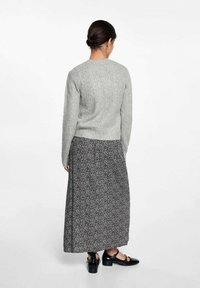 Světle šedý, žebrovaný svetr, pohled zezadu, spárovaný s dlouhou černou sukní s květinovým vzorem a černými botami na řemínky. Hladká textura, ležérní design.