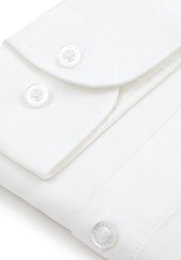 Biała torba z tkaniny, z widocznymi metalowymi zapięciami zatrzaskowymi, przezroczystym guzikiem i gładką, teksturowaną powierzchnią. Prosty projekt klapki.