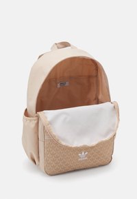 Béžový batoh s texturovaným květinovým vzorem na přední kapse, hladkým vnitřkem a nastavitelnými popruhy. Na přední straně logo Adidas.