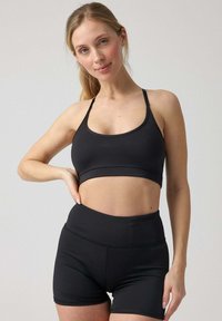 Bra sportivo nero con spalline sottili, caratterizzato da un ampio elastico; abbinato a pantaloni corti neri a vita alta, entrambi realizzati in materiale elasticizzato.