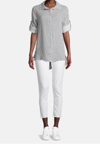 Camicia a righe bianca e nera, con maniche arrotolate e una vestibilità rilassata, abbinata a pantaloni cropped bianchi e sneakers bianche.