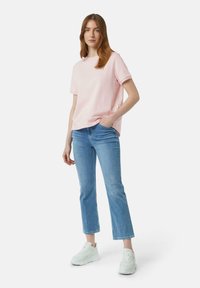 Lichtroze katoenen T-shirt met korte mouwen, ronde halslijn en een relaxte pasvorm, gecombineerd met lichtblauwe rechte jeans en witte sneakers.