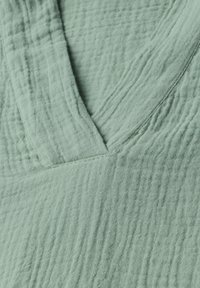 Tessuto verde chiaro, texture con una superficie leggermente rugosa e design a v. Dettagli di cucitura visibili lungo i bordi.