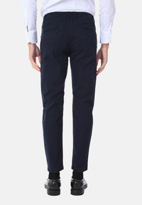 Chino in cotone blu navy con vestibilità slim, dotati di tasche posteriori e passanti per cintura. Texture liscia e gambe affusolate, abbinati a scarpe nere.