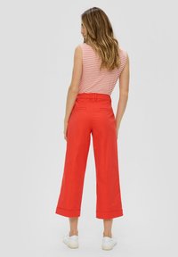 Czerwone szerokie spodnie z wysokim stanem i podwiniętymi mankietami, w zestawieniu z paskowaną bluzką bez rękawów, noszone z białymi sneakersami.
