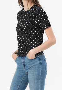 Camisa negra de manga corta con lunares blancos, textura acanalada, cuello redondo, combinada con jeans ajustados de un azul claro.