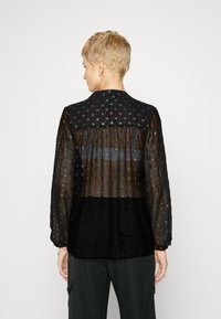 Svart gjennomsiktig bluse med flerfarget blomsterbroderi, lange ermer, høy krage og samlet ryggdetalj, med en helsvart nedre del.
