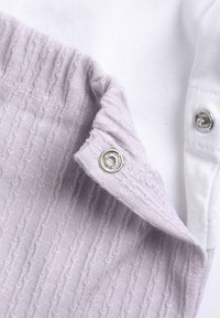 Tessuto di cotone lilla con texture a costine e dettaglio con chiusura a scatto, abbinato a una sezione di cotone bianco liscio. La vista ravvicinata mette in evidenza la texture.