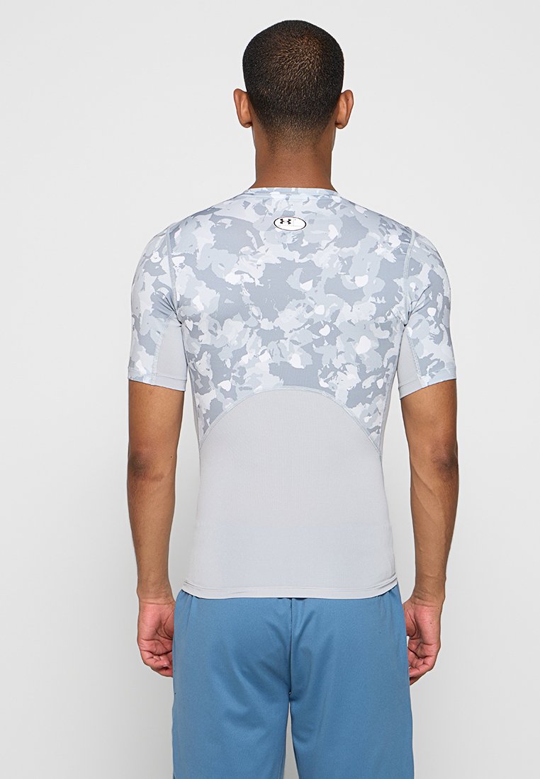 Camisa de compresión gris y blanca con mangas cortas, que presenta un patrón de camuflaje en la parte trasera y un diseño ajustado y suave. Logotipo en el escote.