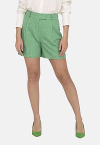 Shorts de lino verde con un patrón texturizado, cintura alta y detalle plisado en la parte delantera. Combinados con zapatos de tacón verde para crear contraste.