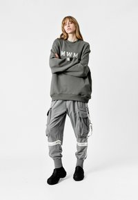 Sudadera gris con letras "MWM", combinada con pantalones cargo grises que tienen múltiples bolsillos y acentos a rayas. Calzado texturizado negro.