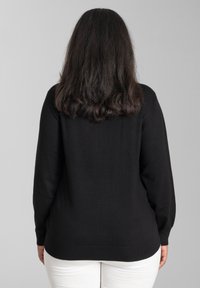 Schwarzer Pullover mit langen Ärmeln und Rundhalsausschnitt, der eine glatte Textur und einen gerippten Saum aufweist. Getragen mit hellen Hosen.