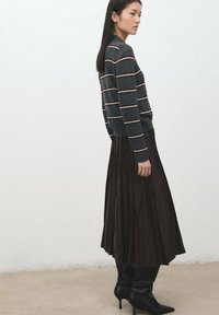 Maglione a righe grigio scuro con dettagli color crema, abbinato a una gonna plissettata marrone scuro e stivali neri con tacco fino al ginocchio. Tessuto liscio.